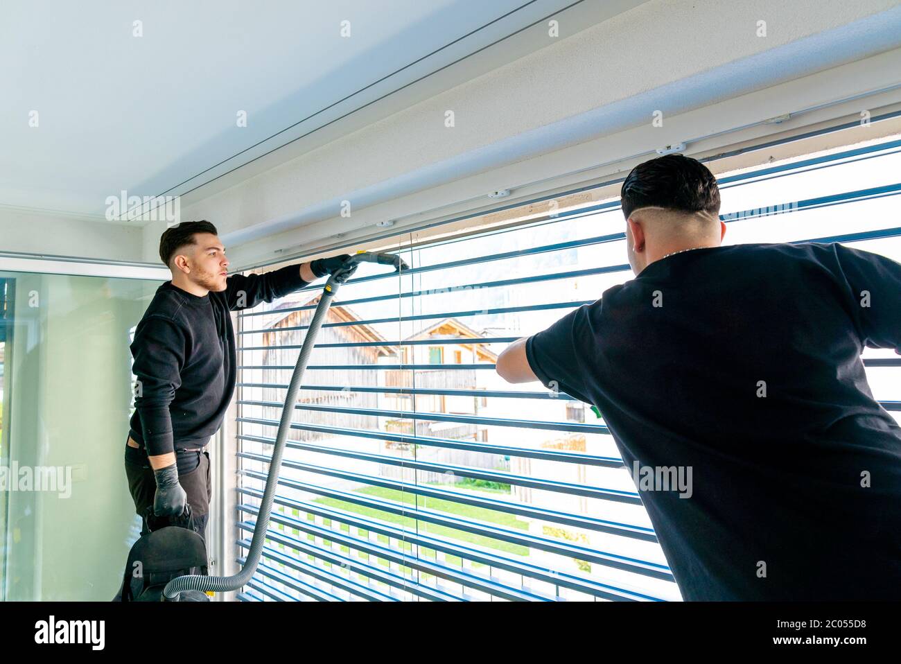 Horizontale Ansicht von zwei männlichen professionellen Reinigern Reinigung Jalousien auf einer großen Fensterfront mit Mikrofasertüchern Stockfoto