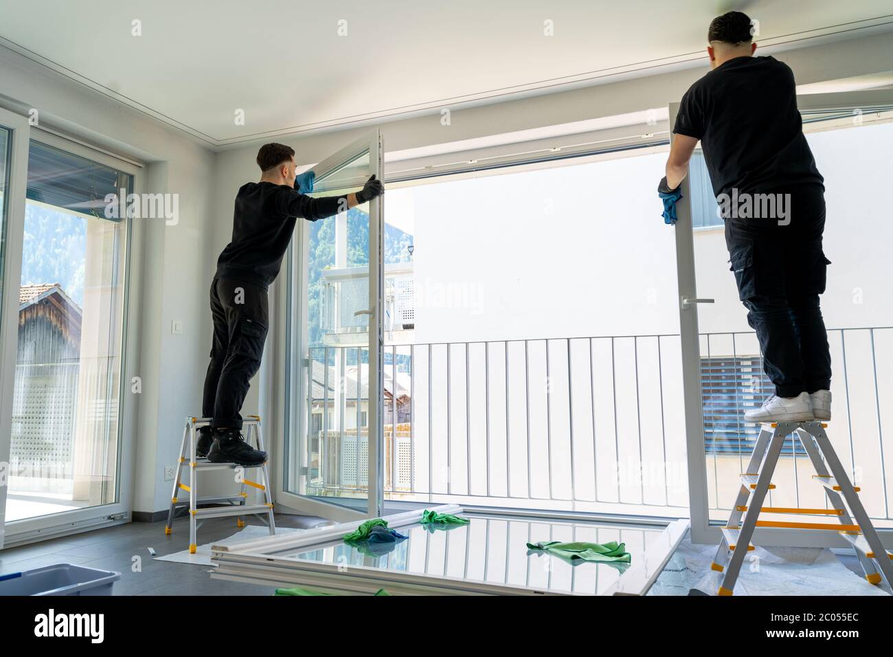 Horizontale Ansicht von zwei männlichen professionellen Reinigern Reinigung Jalousien auf einer großen Fensterfront mit Mikrofasertüchern Stockfoto