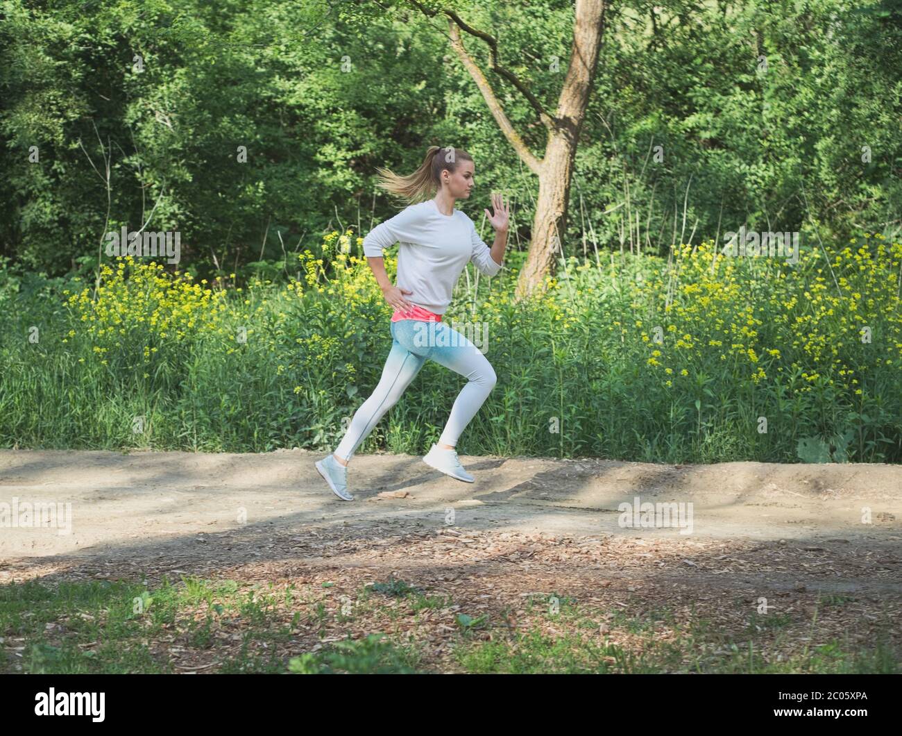 Junge Blonde kaukasische Frau läuft im Wald auf einem Dirt Road Stockfoto