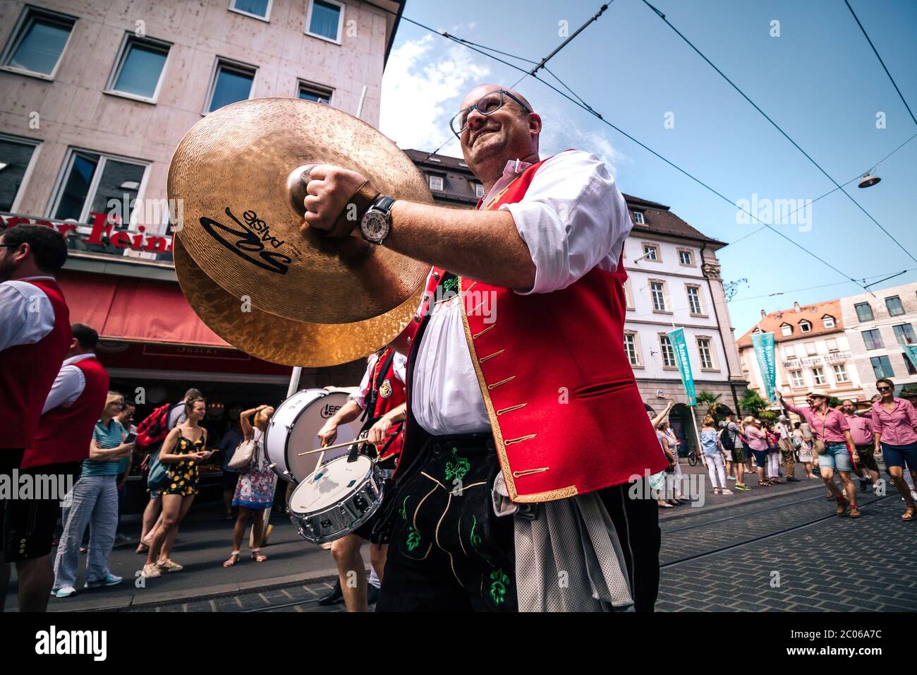 Rot gekleideter Messingmusiker mit riesigen Handbellen in typischer Volkskostüme aus dem Dorf Püssensheim bei der Eröffnungspartade des Kiliani Sommerfair. Stockfoto