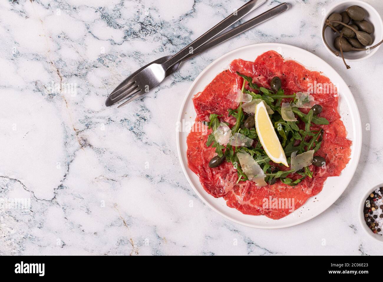 Marmorierte Rind-Carpaccio mit Rucola, Kapern, Zitrone und Parmesan, Draufsicht Stockfoto