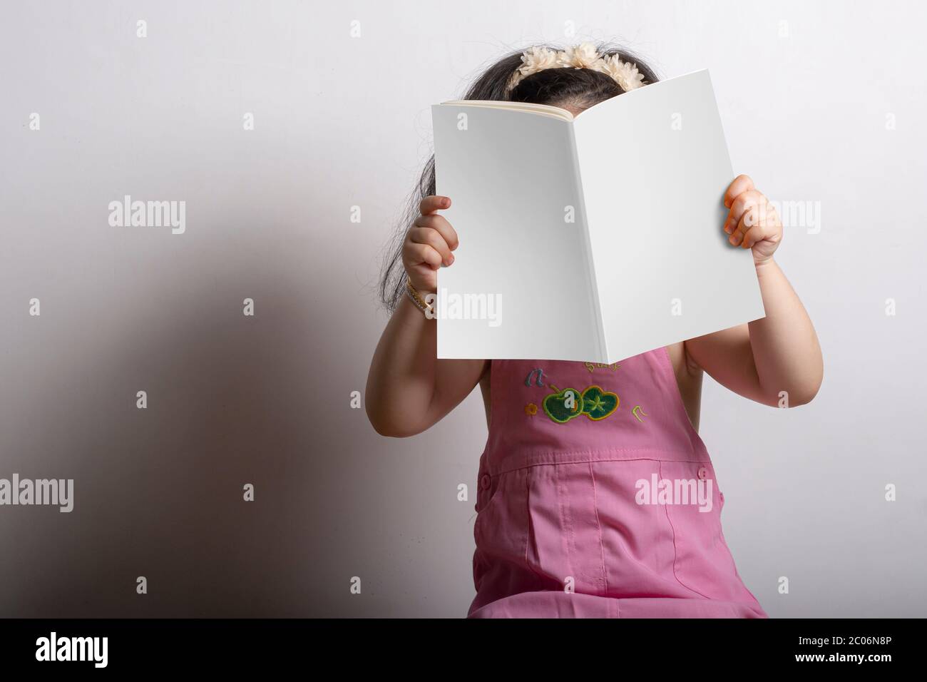 Kleines Mädchen hält ein Kinder-Geschichte-Buch mit leerem Cover vor ihrem Gesicht, editierbare Modell bis Vorlage bereit für Ihr Design, Abdeckung Auswahlpfad Stockfoto
