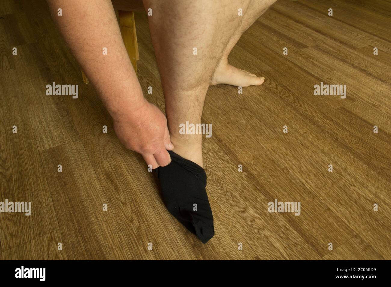 Herrenhände setzen sich schwarze Socken auf die Füße Stockfoto