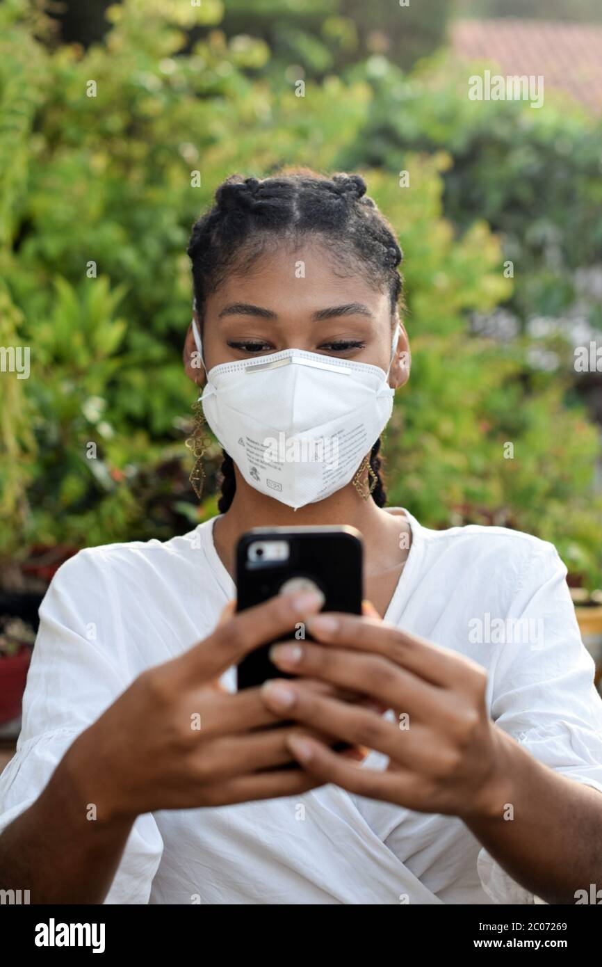 Junge schwarze Frau in Gesichtsmaske mit einem Smartphone Stockfoto