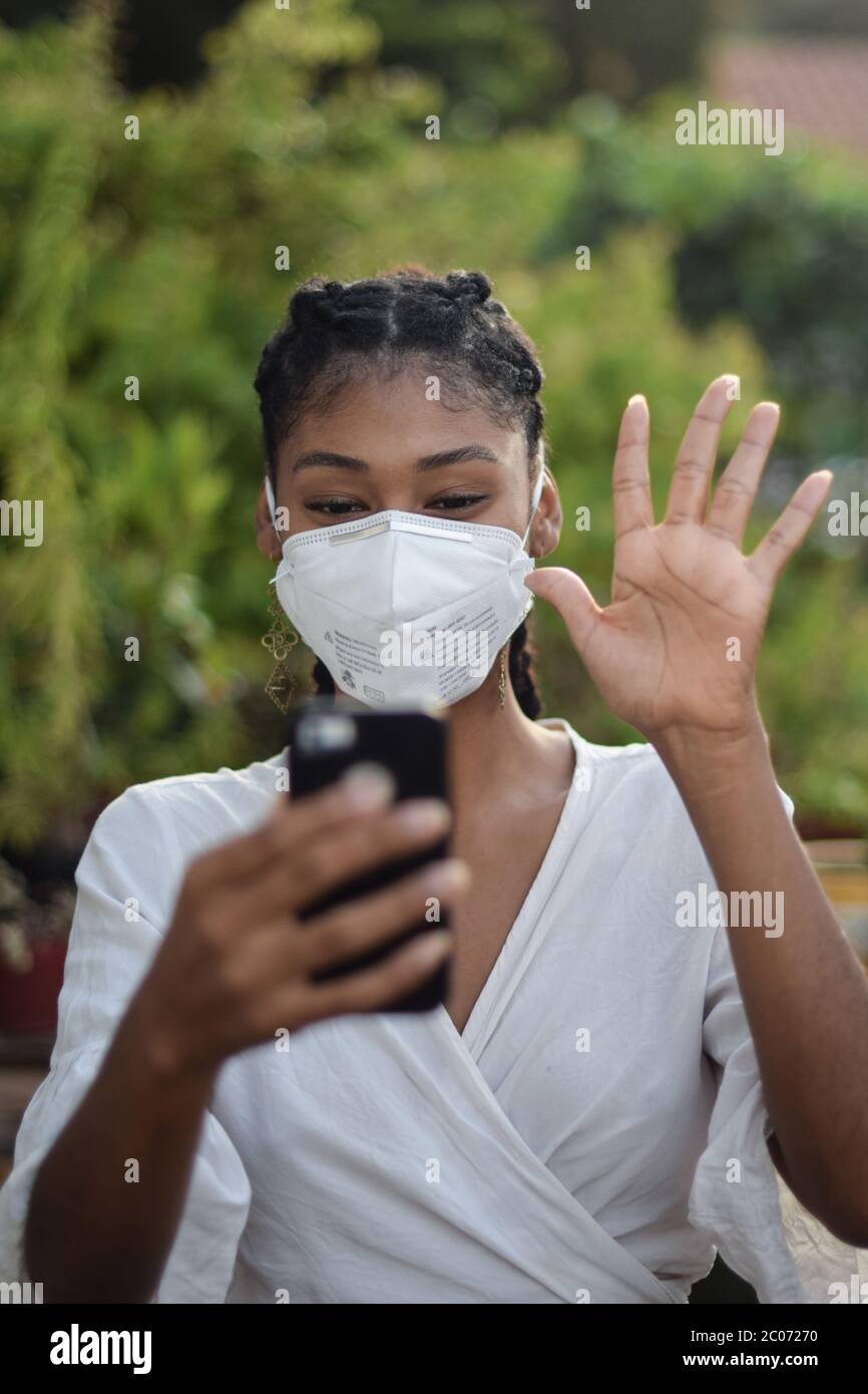 Junge schwarze Frau in Gesichtsmaske einen Videoanruf zu machen Stockfoto