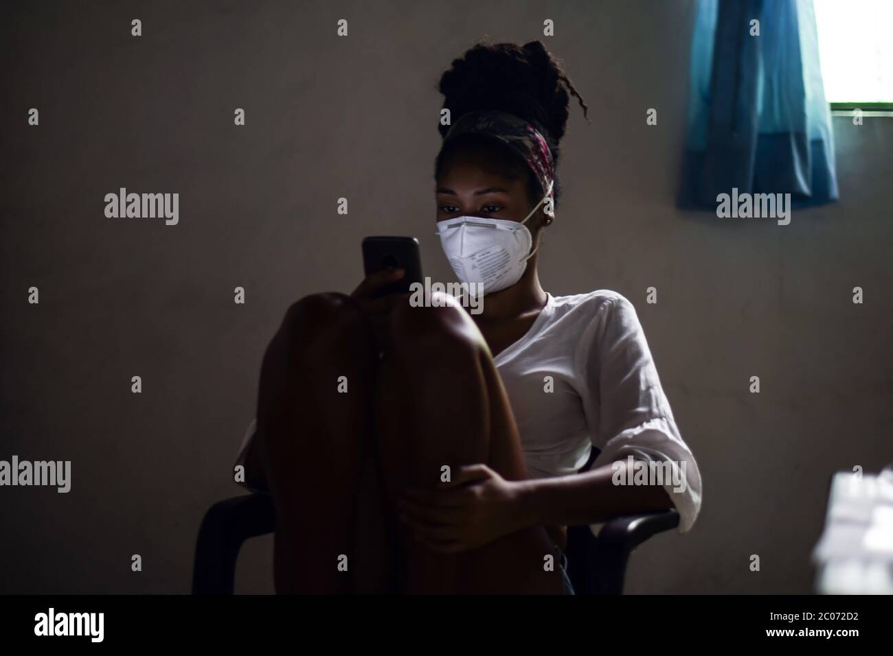 Junge Frau in Gesichtsmaske mit Smartphone im dunklen Raum Stockfoto