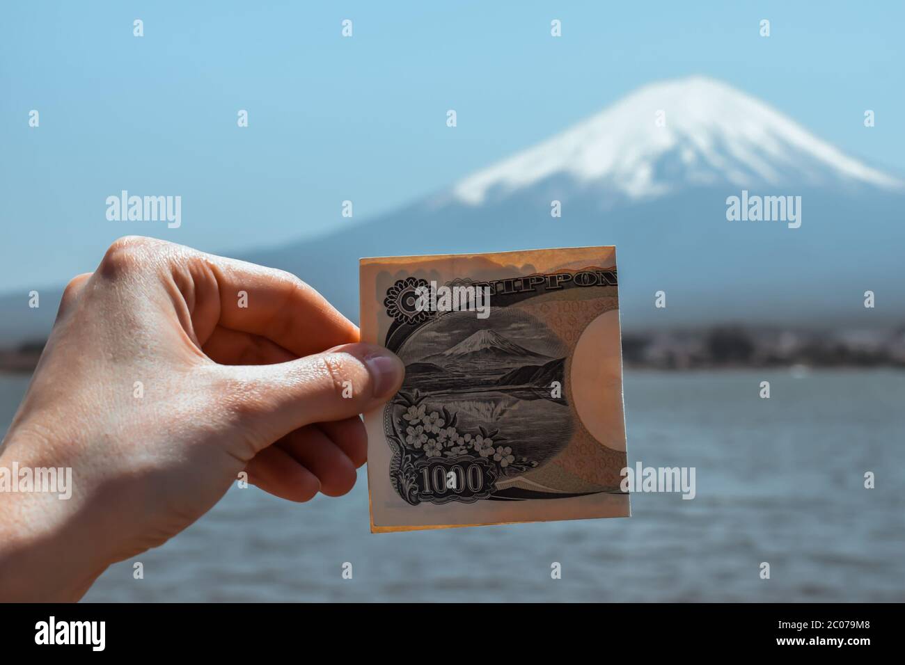 Eine weibliche Hand mit einer 1000 Yen Banknote vor dem Fuji-Berg, um die Ähnlichkeit in Kawaguchiko Japan zu zeigen Stockfoto