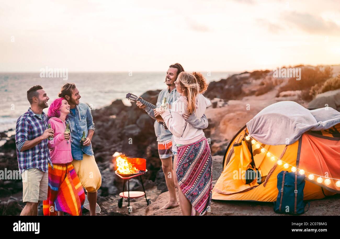 Gruppe glückliche Freunde Spaß beim Camping im Freien - Junge Leute Bier trinken und Gitarre spielen auf dem Campingplatz neben dem Strand Stockfoto