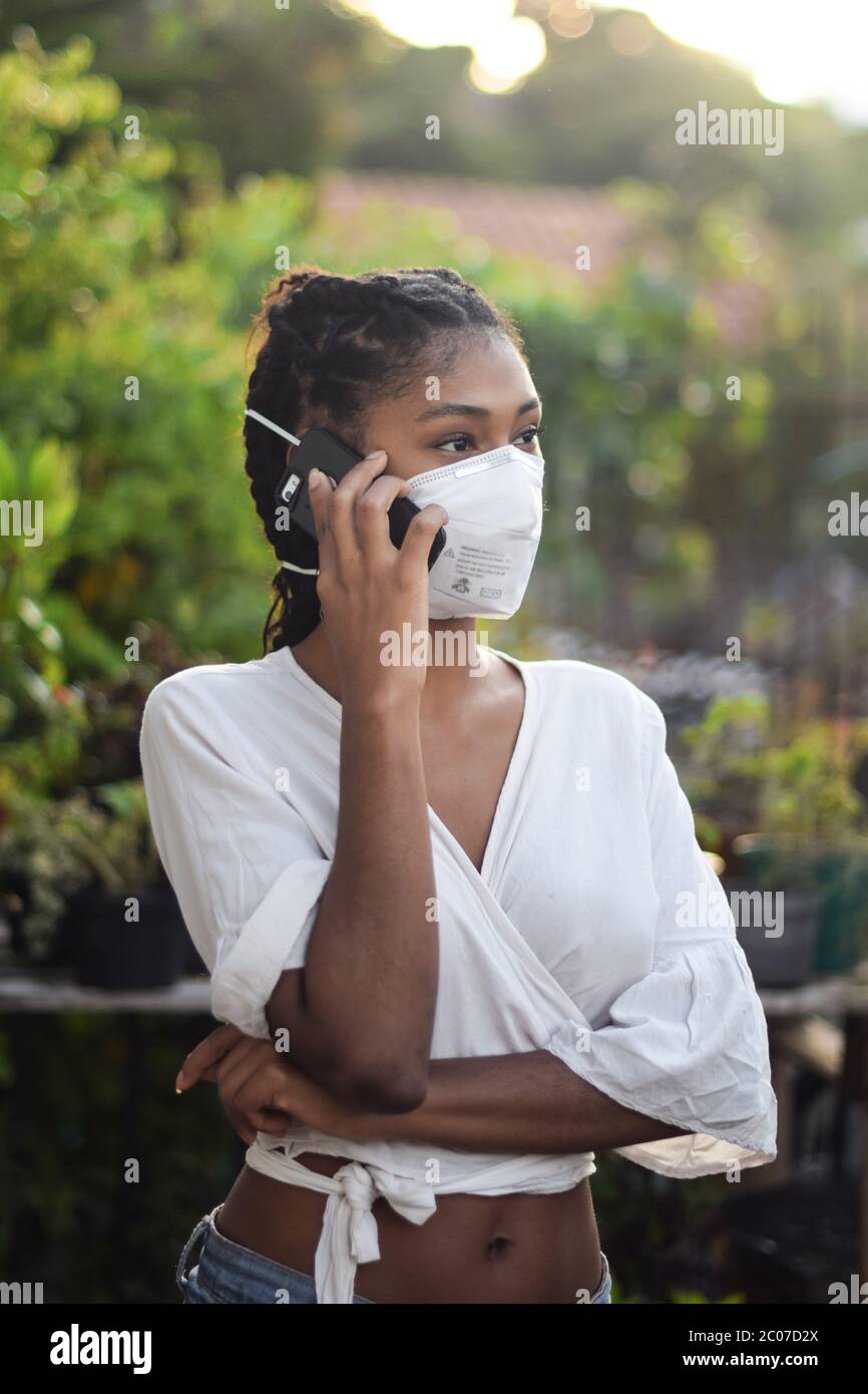 Junge schwarze Frau in Gesichtsmaske sprechen am Telefon Stockfoto