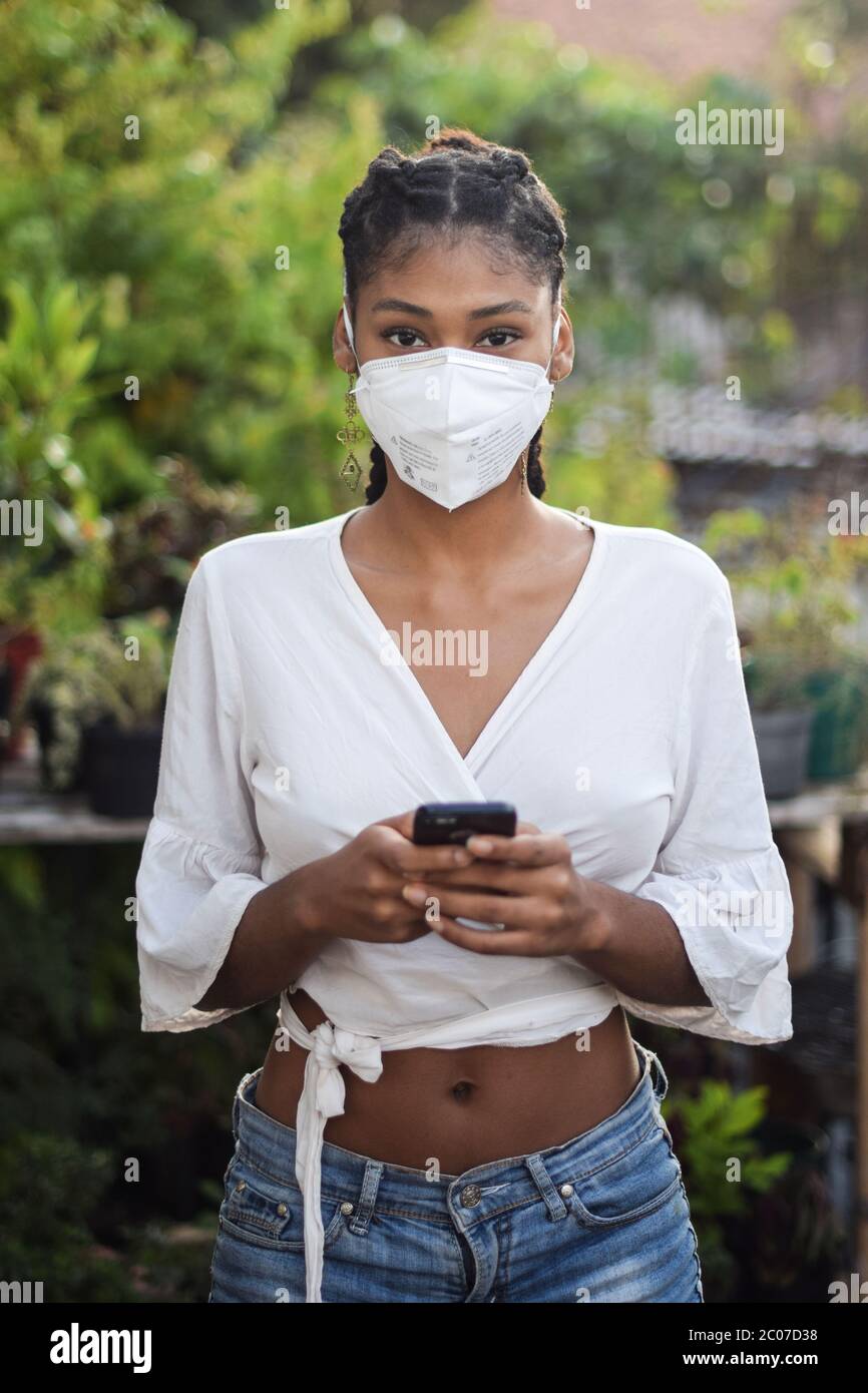 Junge schwarze Frau in Gesichtsmaske mit einem Smartphone Stockfoto