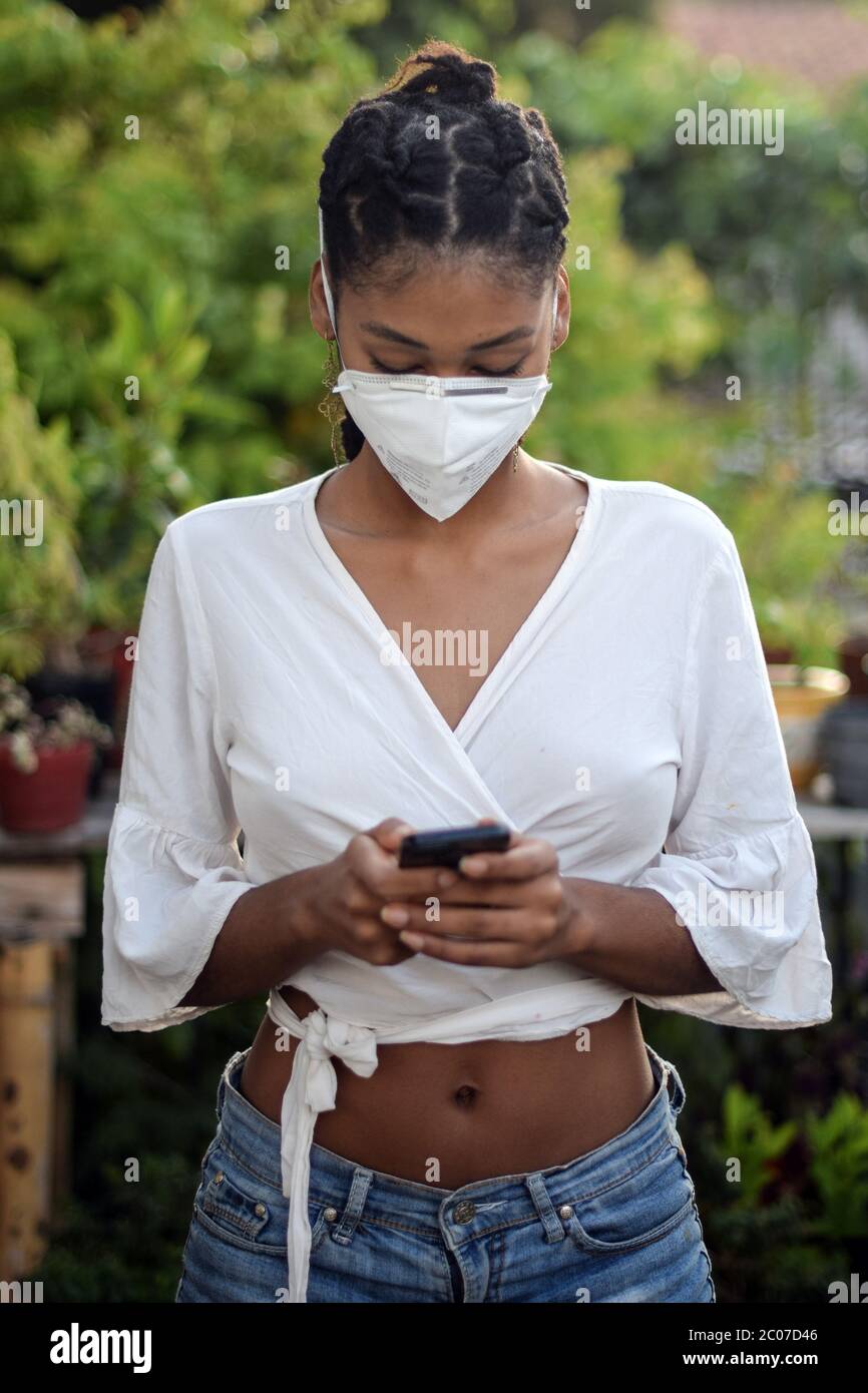 Junge schwarze Frau in Gesichtsmaske mit einem Smartphone Stockfoto