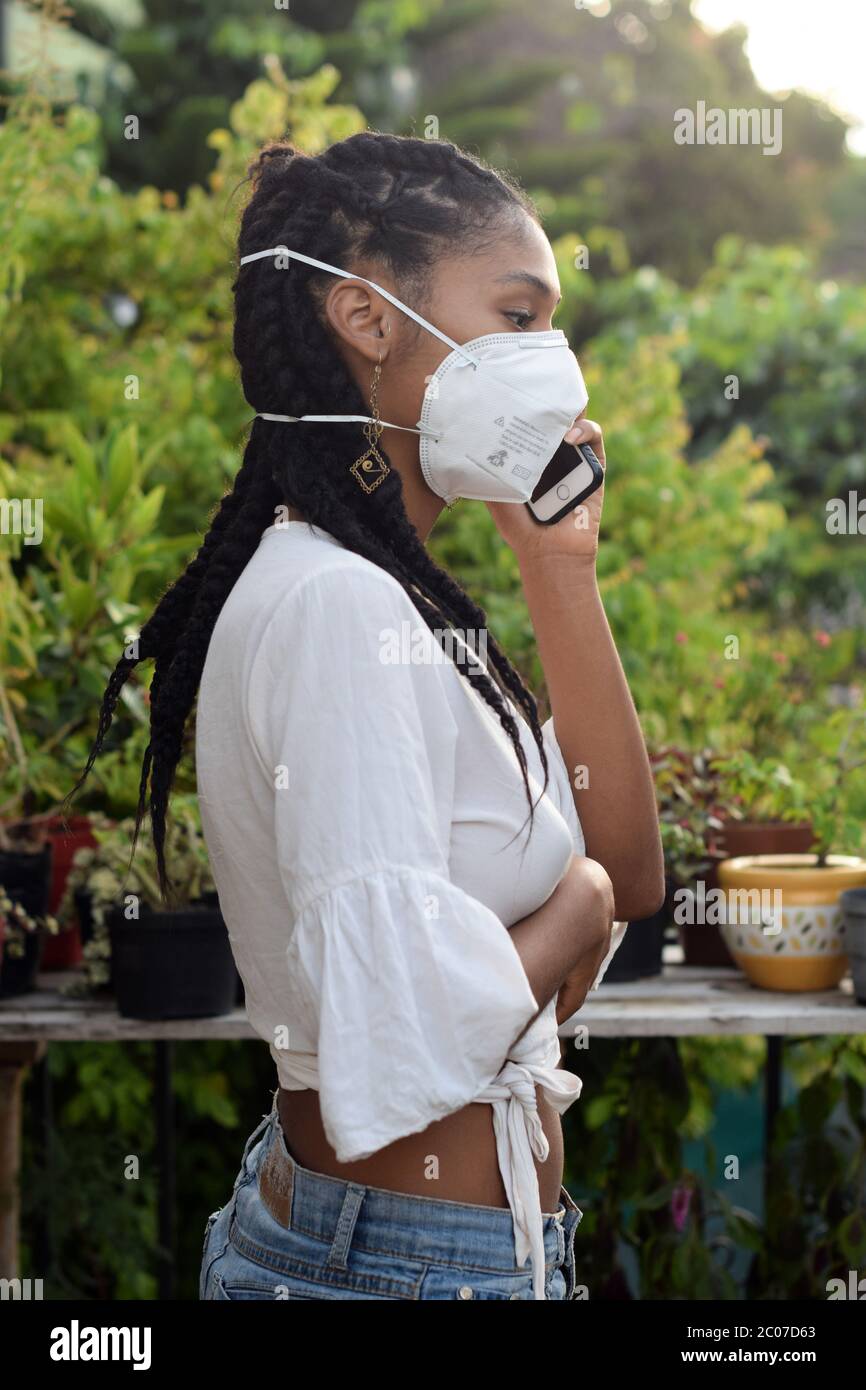 Junge schwarze Frau in Gesichtsmaske sprechen am Telefon Stockfoto