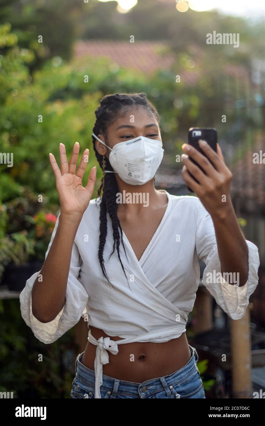 Junge schwarze Frau in Gesichtsmaske einen Videoanruf zu machen Stockfoto