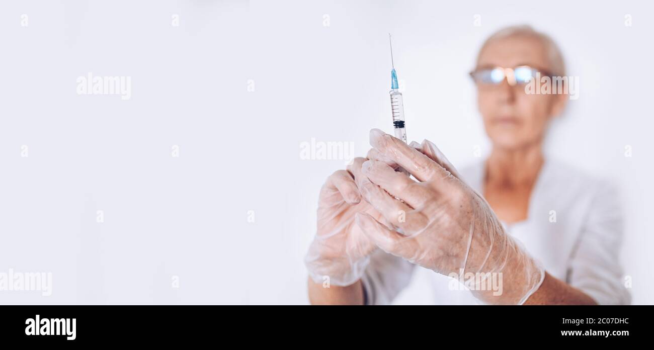 Ältere ältere Frau Arzt oder Krankenschwester mit Spritze in einem weißen medizinischen Mantel und Handschuhe tragen persönliche Schutzausrüstung isoliert. Gesundheitswesen und med Stockfoto