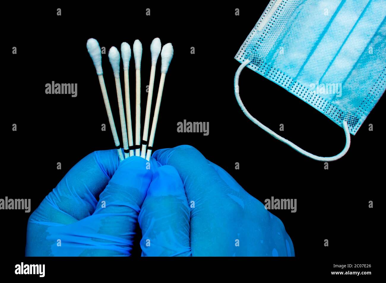Eine Nahaufnahme von Händen, die Handschuhe tragen, zu einem medizinischen Personal, das die Kehle hält, Tupfer neben einer medizinischen Gesichtsmaske auf schwarzem Hintergrund. Stockfoto