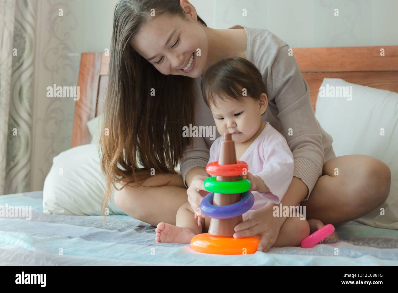 Ein Elternteil hilft ihr Kleinkind stapeln Ring Schleifen Lehre Koordination Fähigkeiten. Stockfoto