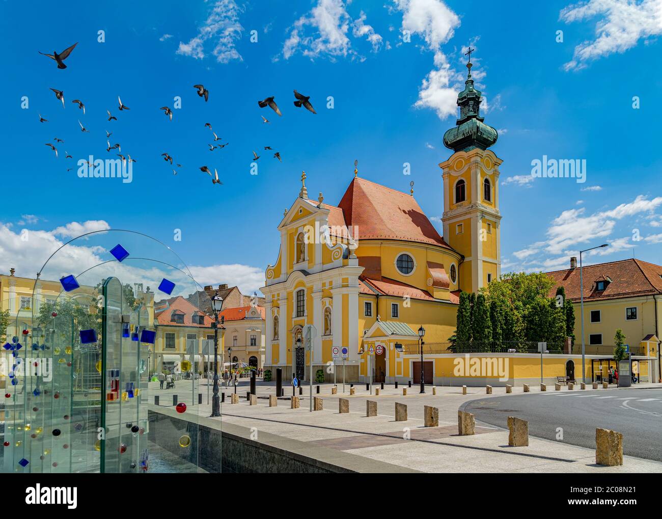 Farbenfroh geschmückter Brunnen und die Karmelitenkirche am Wiener Torplatz in Gyor, Ungarn. Stockfoto