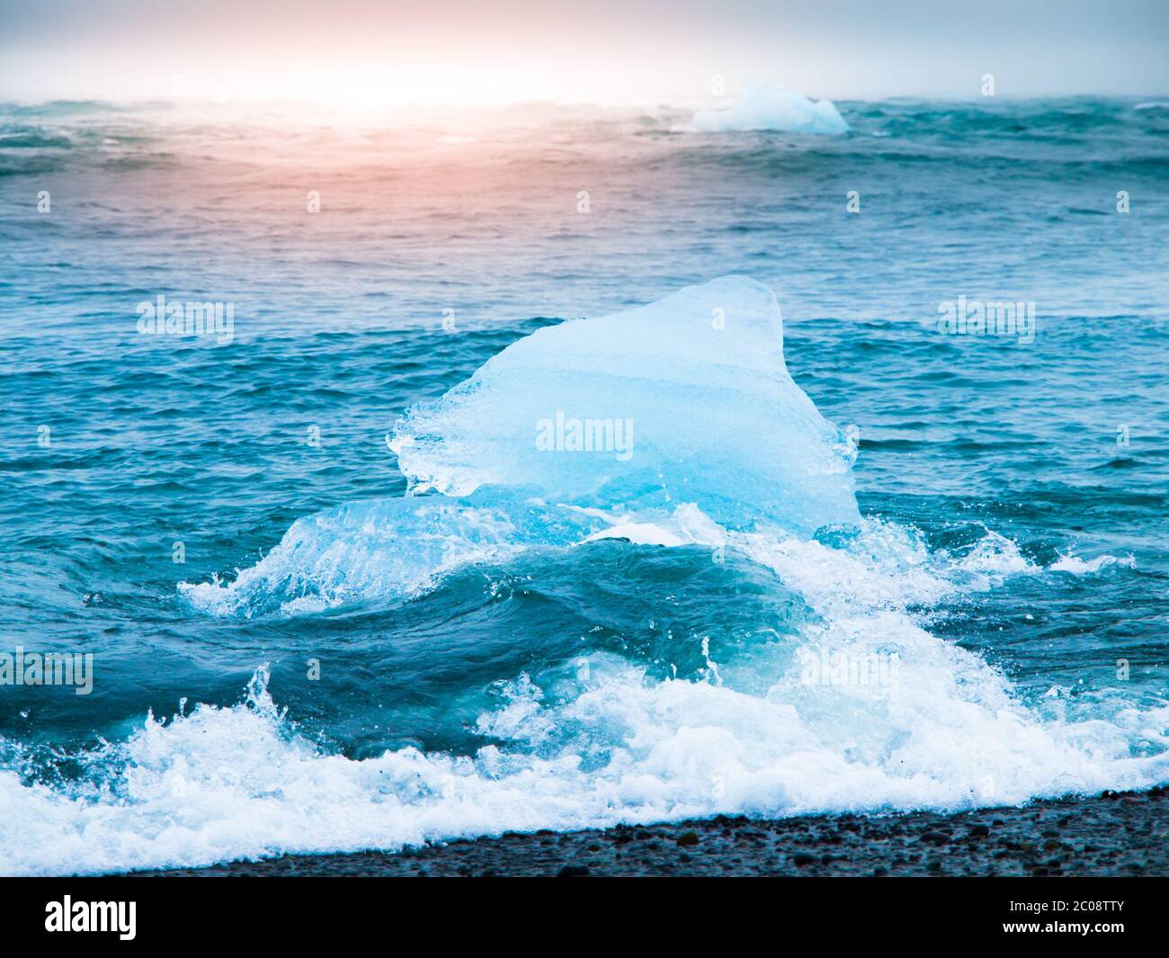 Eisberge, die bei Sonnenaufgang am schwarzen Strand in der Nähe des Jokulsarlon Gletschersees, Island, von Meereswellen überspült werden. Stockfoto