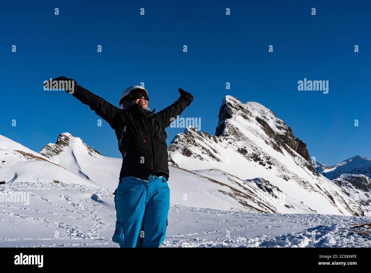 Mädchen genießen Wintersonnenstrahlen mit offenen Armen auf der Spitze der Bergkette. Snowboarder am späten Nachmittag in den Schweizer alpen im Winter. Nahaufnahme und Kontra Stockfoto