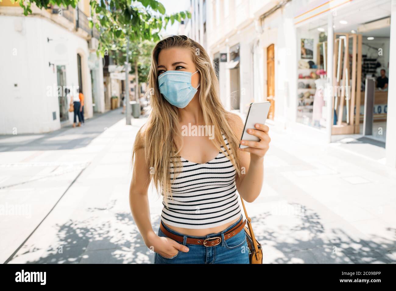 Frau in Maske in der Stadt mit ihrem Handy während der Coronavirus-Pandemie Stockfoto