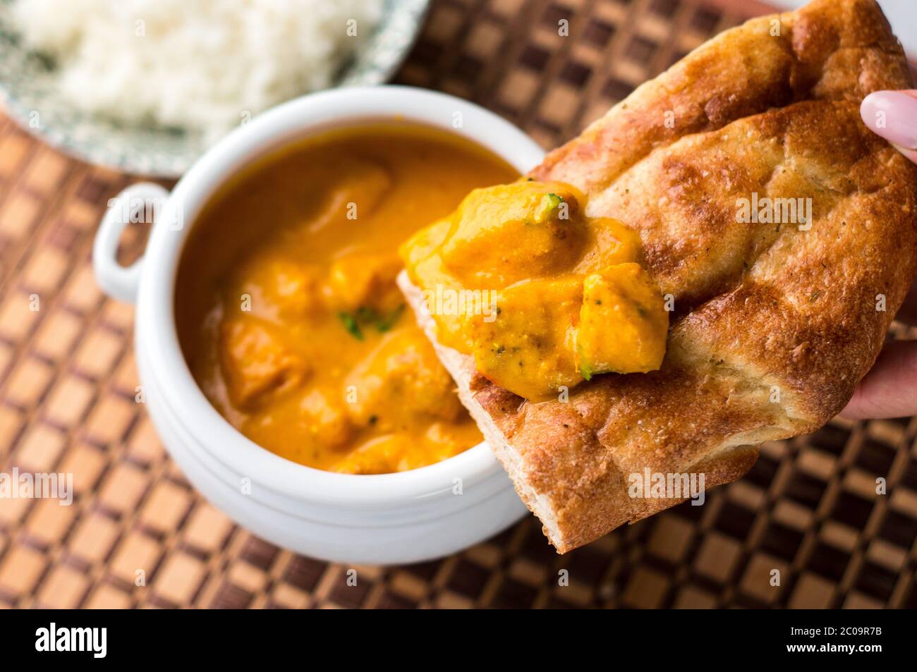 Nahaufnahme von einem leckeren indischen Butter-Hühnercurry auf einem Naan-Brot mit Reis auf einem hölzernen Tischset im Hintergrund. Stockfoto