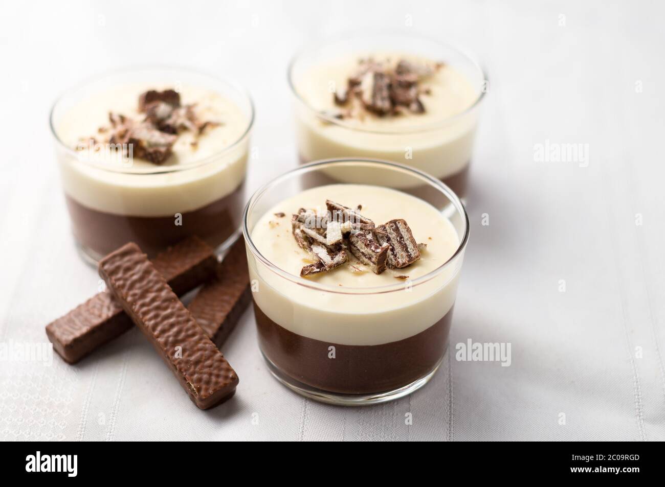 No-bake geschichtete Schokolade Mousse und Käsekuchen mit Schokolade überzogene Wafer Cookie Krümel Belag. In Dessertschüsseln aus klarem Glas. Auf weißem Hintergrund. Stockfoto