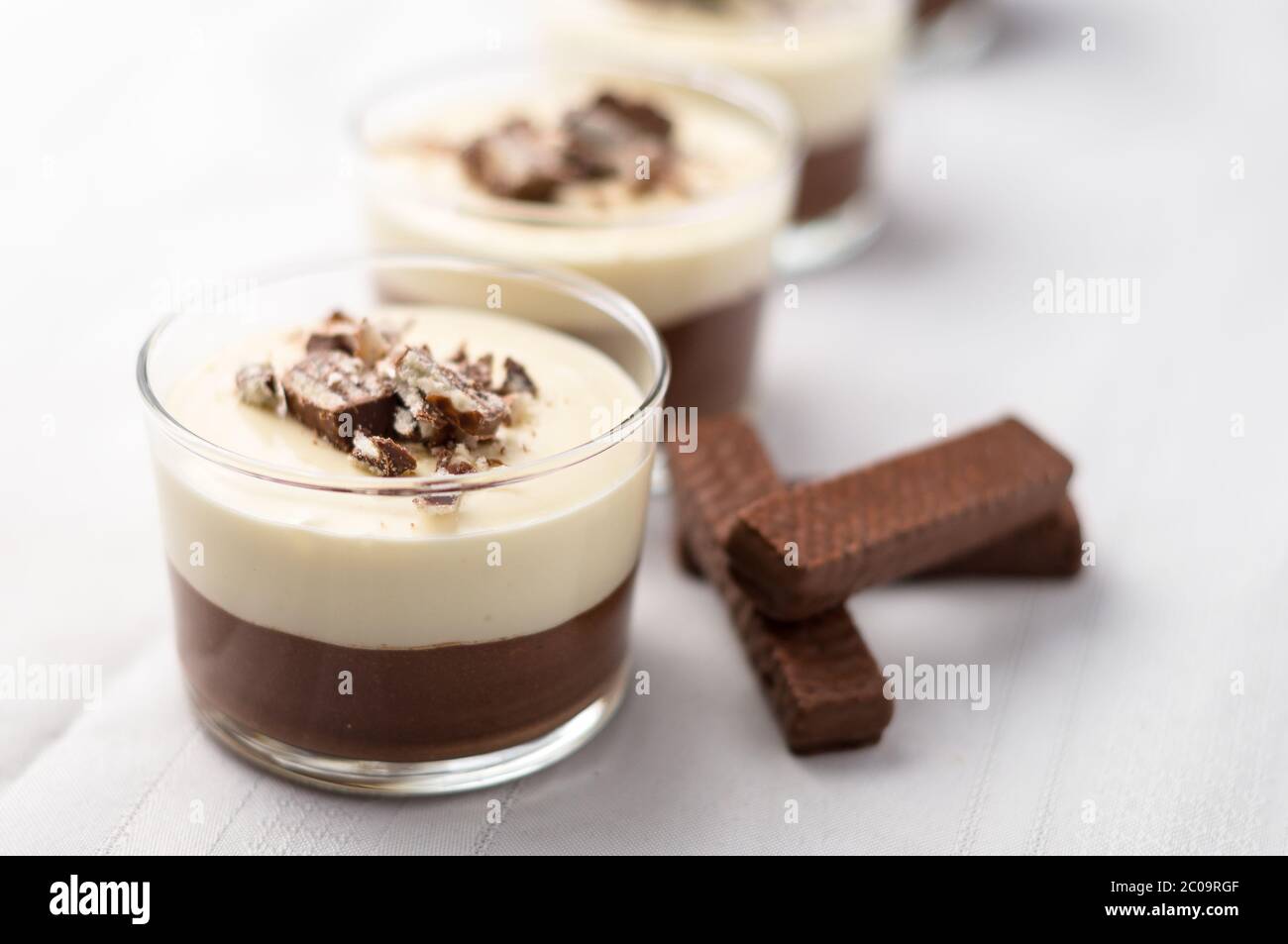 No-bake geschichtete Schokolade Mousse und Käsekuchen mit Schokolade überzogene Wafer Cookie Krümel Belag. In Dessertschüsseln aus klarem Glas. Auf weißem Hintergrund. Stockfoto