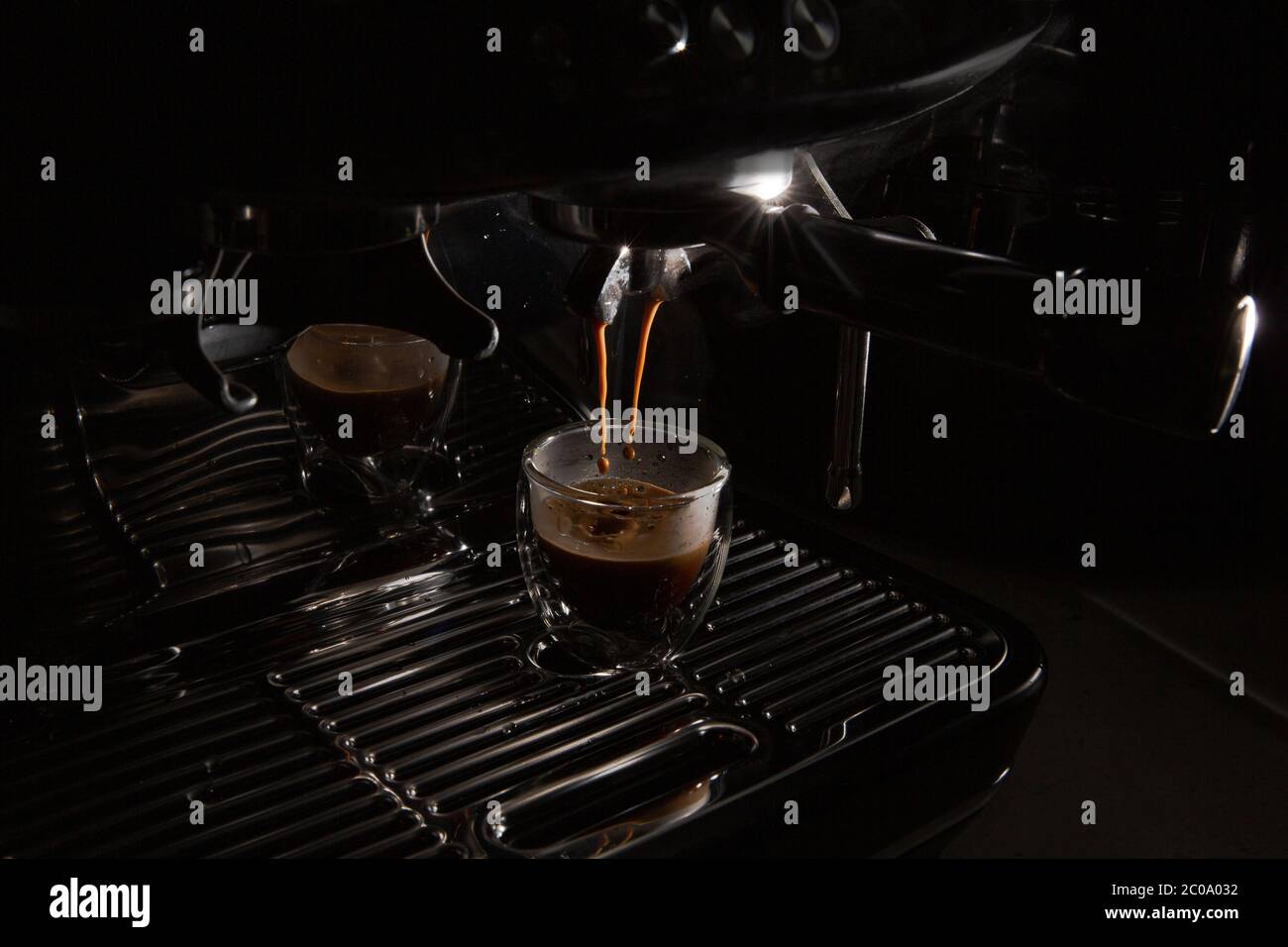 Dunkle Kaffeetropfen tropfen in einer Espressotasse aus transparentem Glas auf einer manuellen Espressomaschine mit Kopierfläche, Nahaufnahme Stockfoto