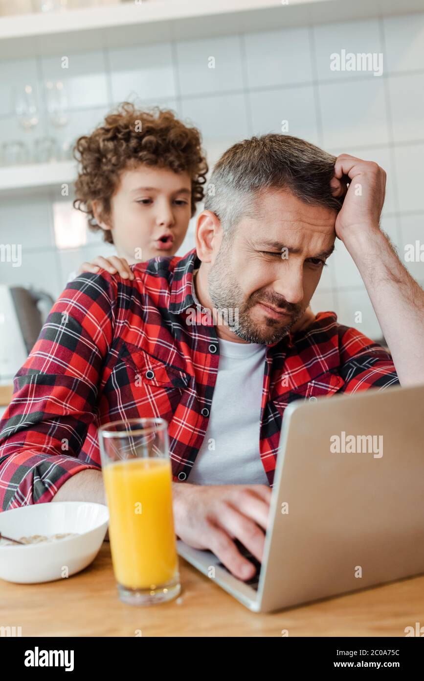 Selektiver Fokus von lockigen und lauten Sohn berühren müde Freelancer Vater von zu Hause aus Stockfoto
