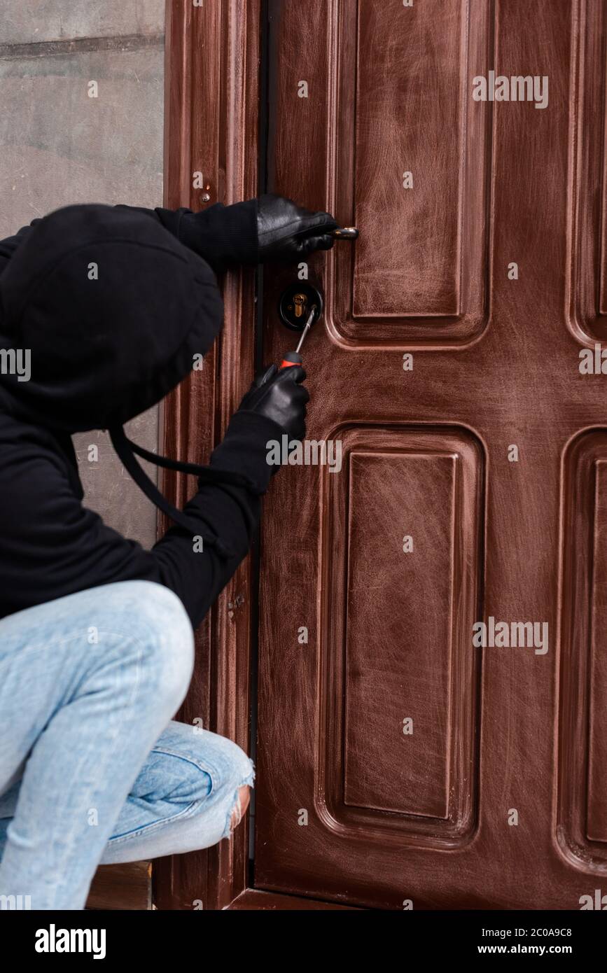 Seitenansicht des Hausbrechers, der das Türschloss mit einem Schraubendreher öffnet Stockfoto