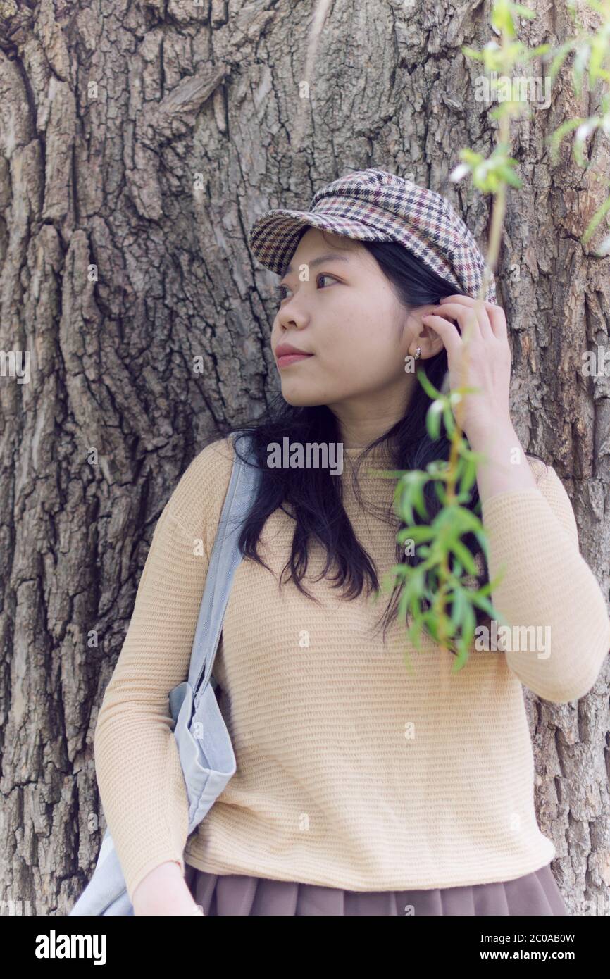 Attraktive asiatische weibliche College Student Blick in die Entfernung während Schiefen gegen EINEN Baum Stockfoto