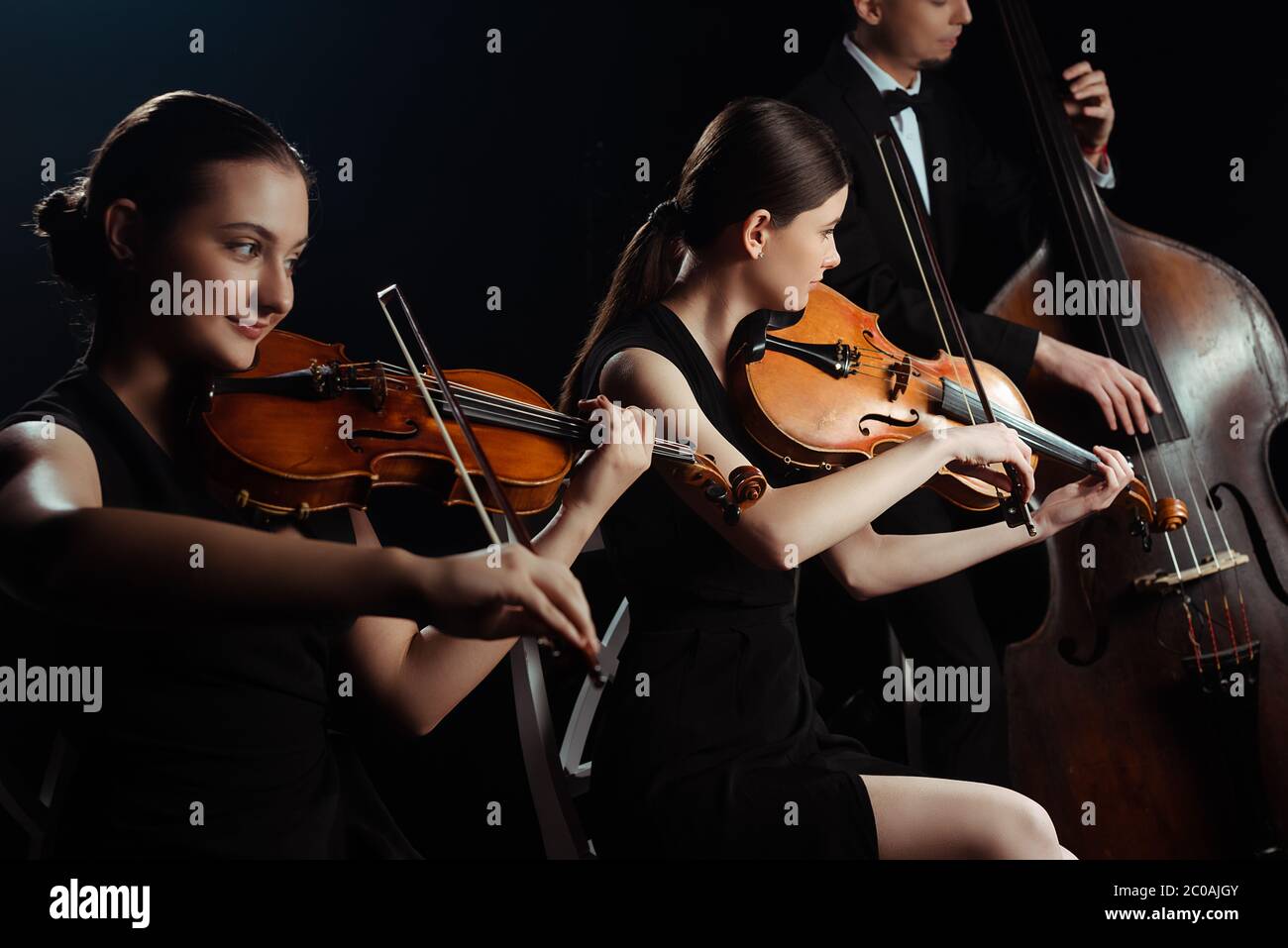 Trio von Musikern, die auf Kontrabass spielen und Violinen isoliert auf Schwarz Stockfoto