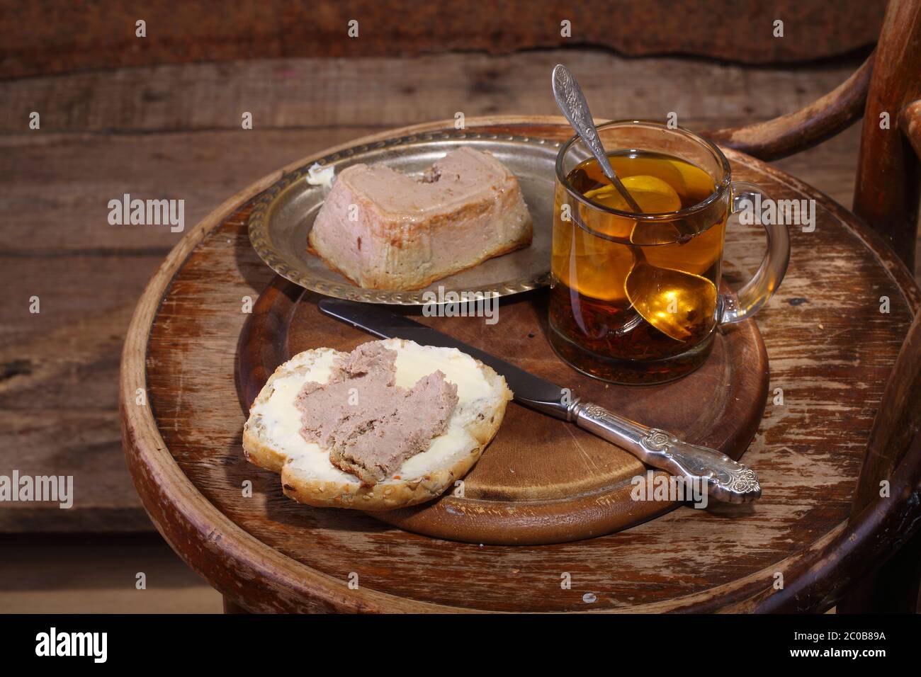 Sandwich mit Fleischpaste und Tee mit einer Zitrone in einem transparenten Becher auf einem Holztisch Stockfoto