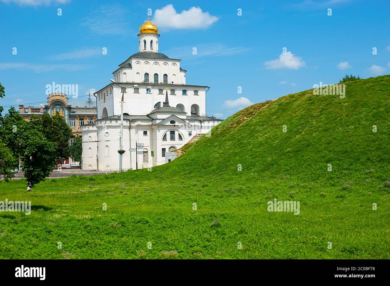 Die Ruinen der mittelalterlichen Erdmauer - Kozlov Val (Stadtmauer), mit Rasen bedeckt vor dem historischen Gebäude des Goldenen Tores mit barbikan Kirche, Stockfoto