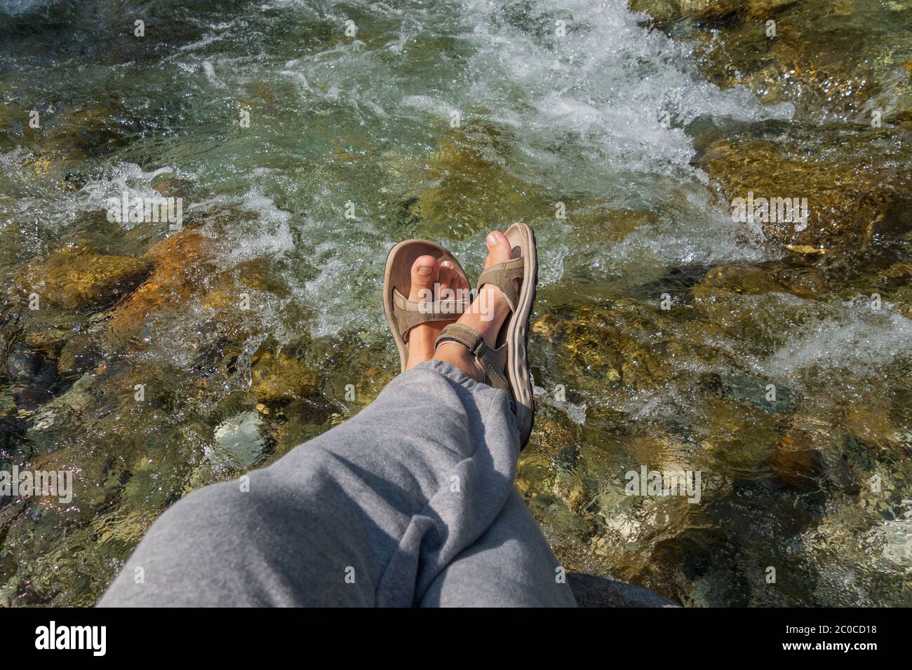 Frauen gebräunte Beine in offenen Sport-Sandalen auf einer Wanderung auf einem Bergfluss im Sommer. Reisekonzept, das Konzept Wandern Stockfoto