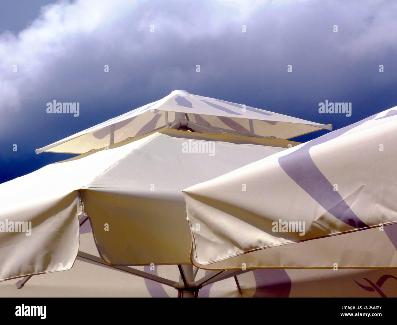 Cremefarbene Leinwand Sonnenschirm und Markise. Blauer und weißer Himmel an einem sonnigen Sommertag. Sonnenschutzkonzept. UV-Exposition. Beige und grau wasserdichte Stoff Stockfoto