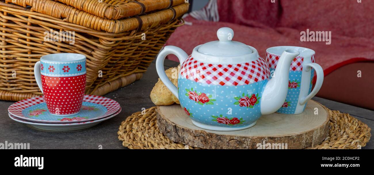 High Tea Picknick-Konzept mit dekorierten Teekanne, Teetassen und Picknickkorb auf einem Tisch Stockfoto