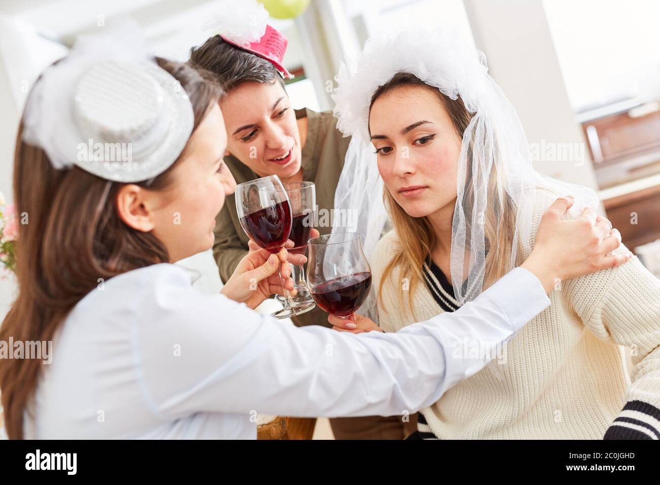 Freundinnen tröstend traurige Braut bei der Hochzeit mit einem Glas Rotwein Stockfoto