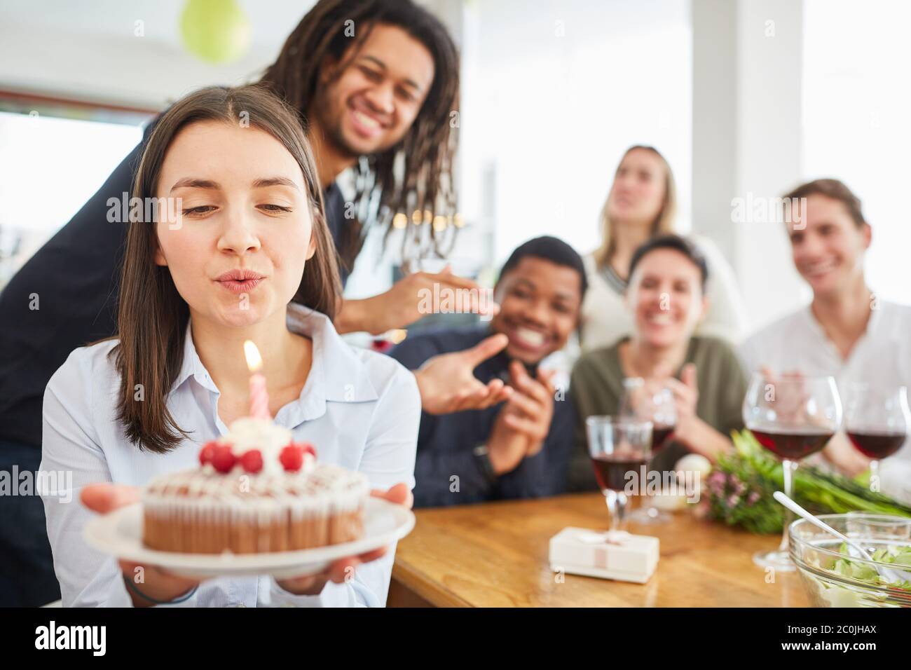 Frau, die Kerze auf Kuchen auf Geburtstagsfeier mit Freunden zu Hause ausblasen Stockfoto
