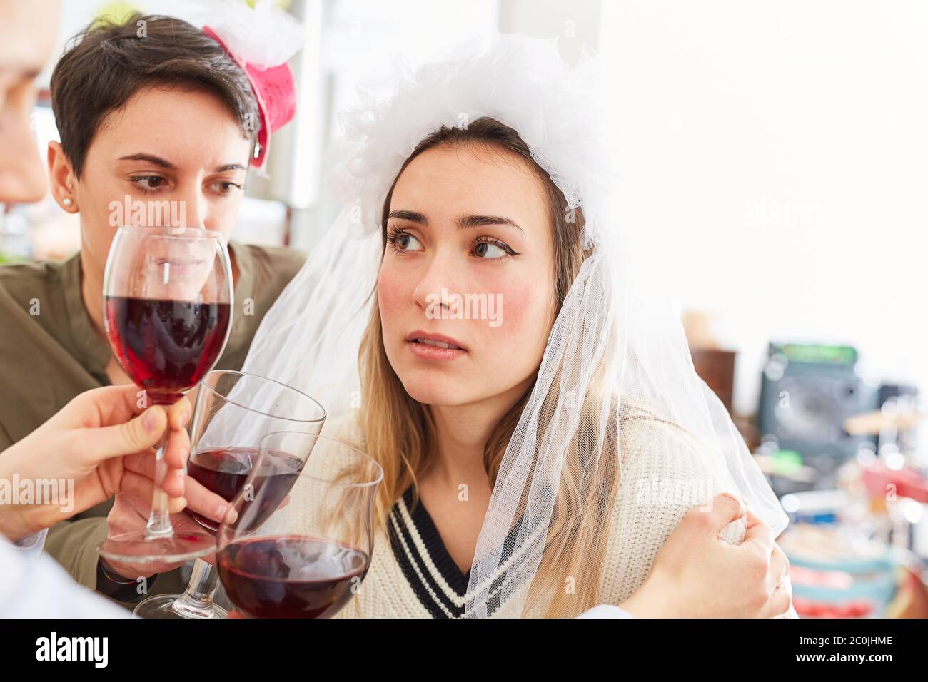Freundinnen trösten enttäuschte Braut nach der Hochzeit mit einem Glas Rotwein Stockfoto