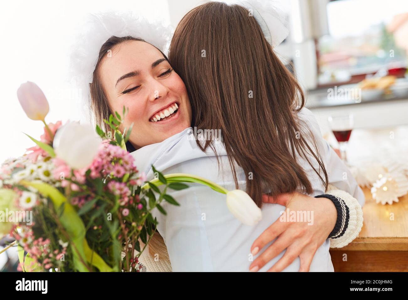 Freundin gratuliert Braut bei der Hochzeit mit Umarmung und Blumenstrauß Stockfoto