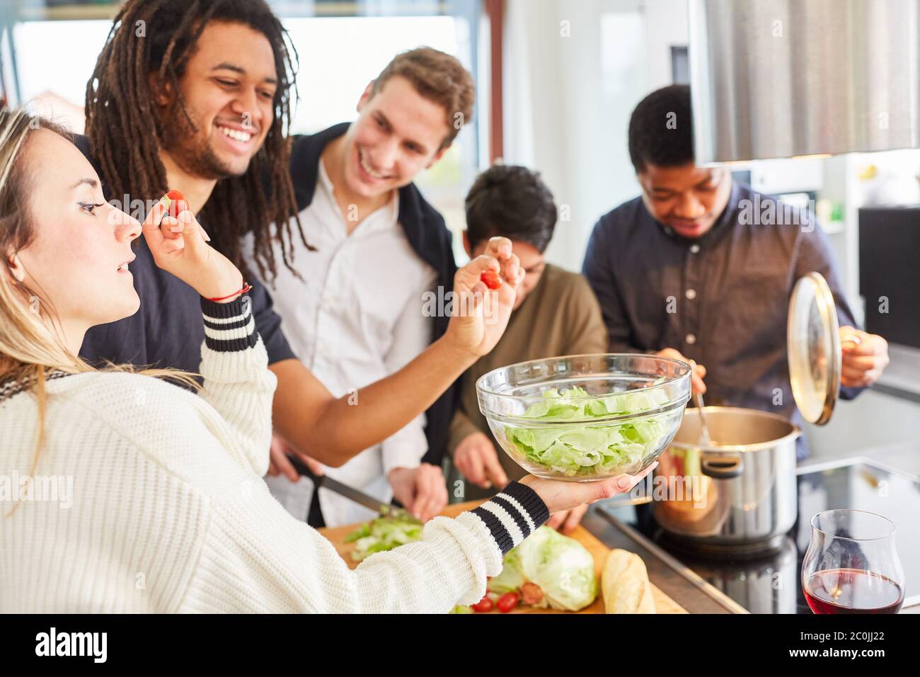 Lachende Studenten bereiten gemeinsam in einer Gemeinschaftsküche Salat zu Stockfoto