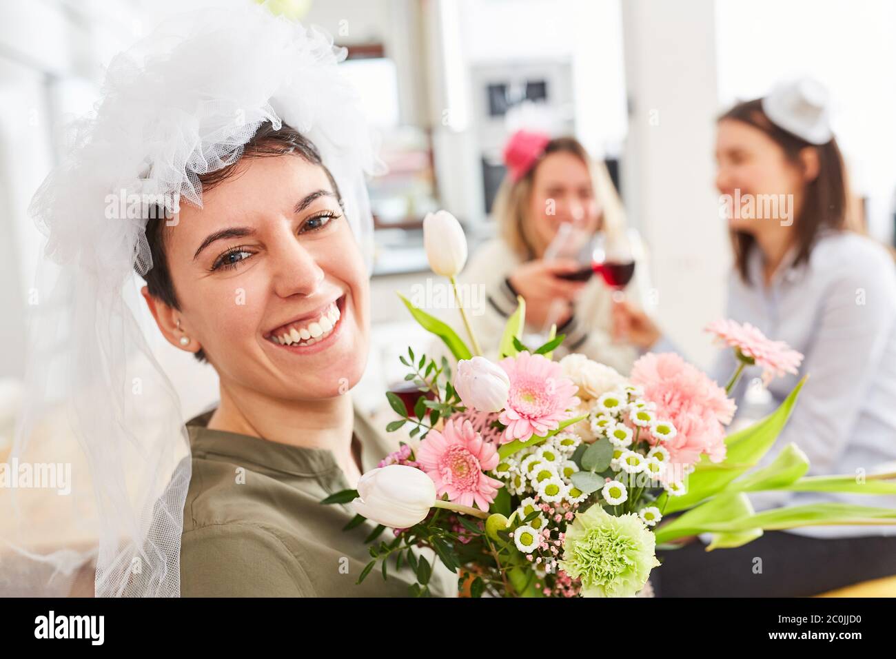 Glückliche Braut mit Brautschleier und Brautstrauß feiert die Hochzeit mit Freunden Stockfoto