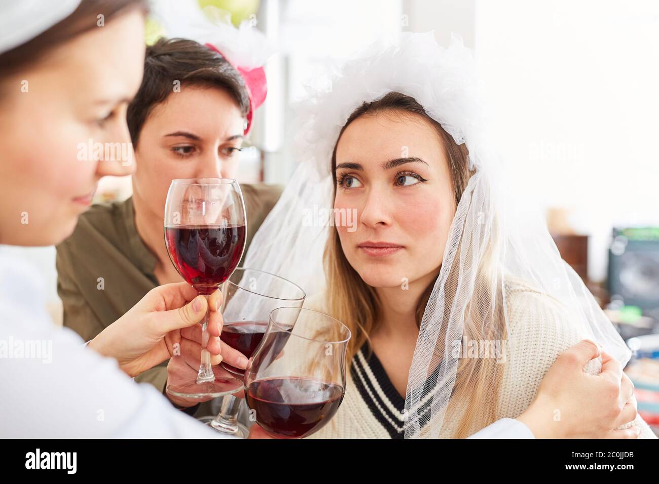 Freunde trösten traurige Braut nach einer enttäuschten Hochzeit mit einem Glas Rotwein Stockfoto