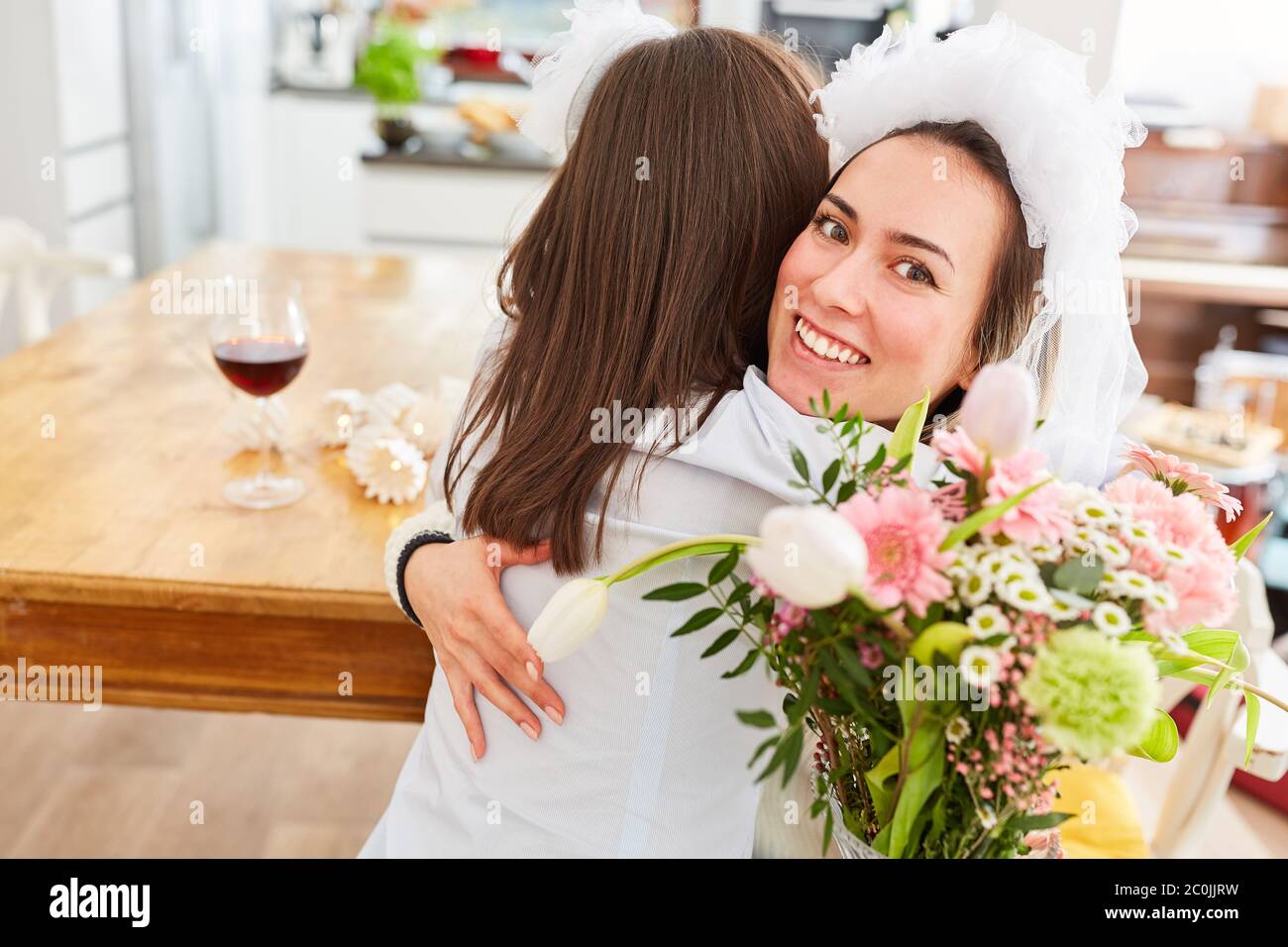 Freundin umarmt glückliche Braut mit Blumenstrauß bei der Hochzeit für Glückwünsche Stockfoto