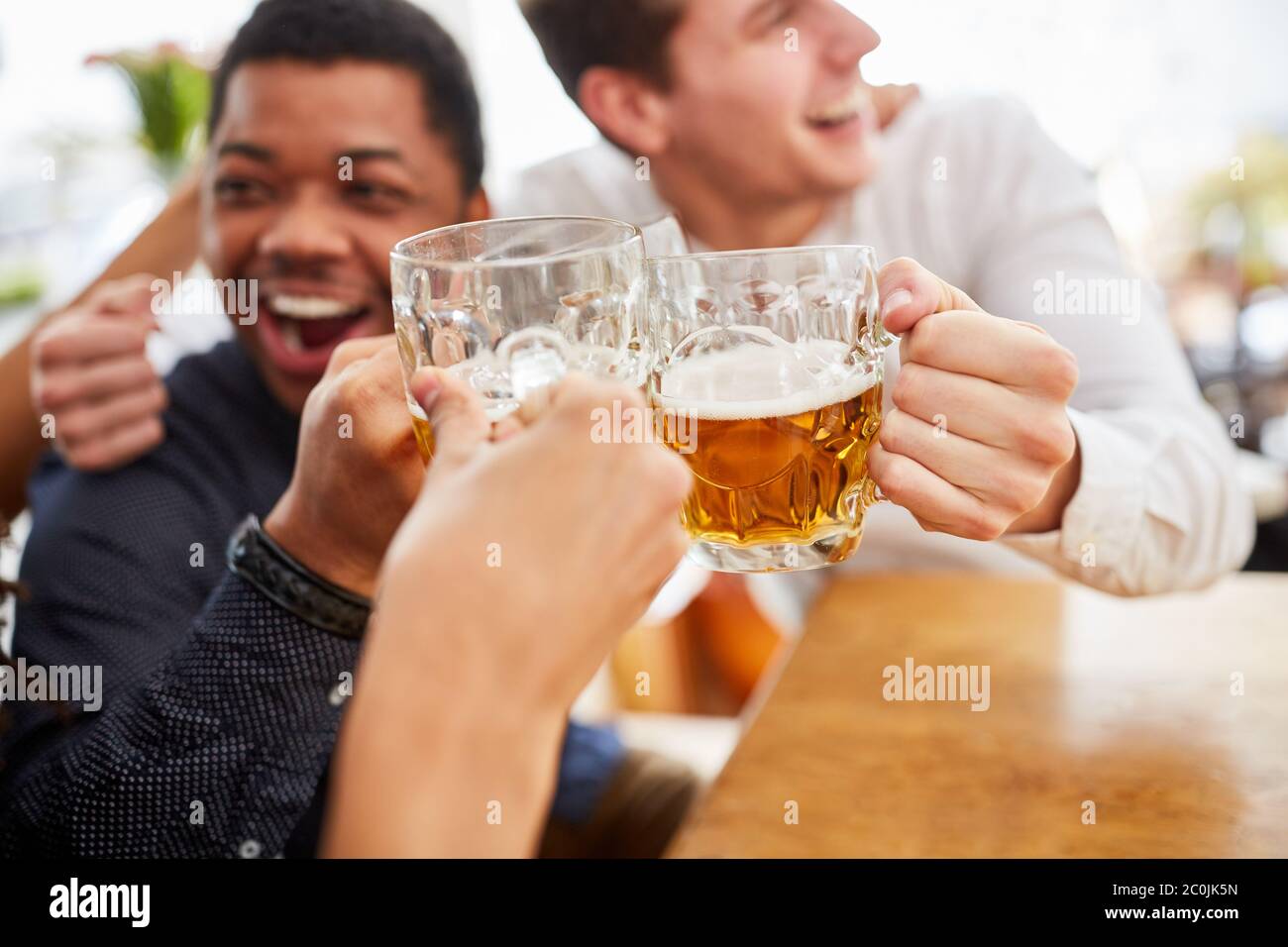 Lachend jubelnde Männer trinken Bier und toasten sich im Biergarten auf dem Oktoberfest Stockfoto