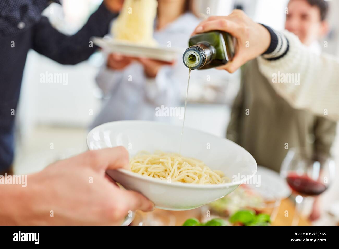 Man gießt Olivenöl auf Spaghetti auf einem Teller, während eine Gruppe von Freunden zu Mittag essen Stockfoto