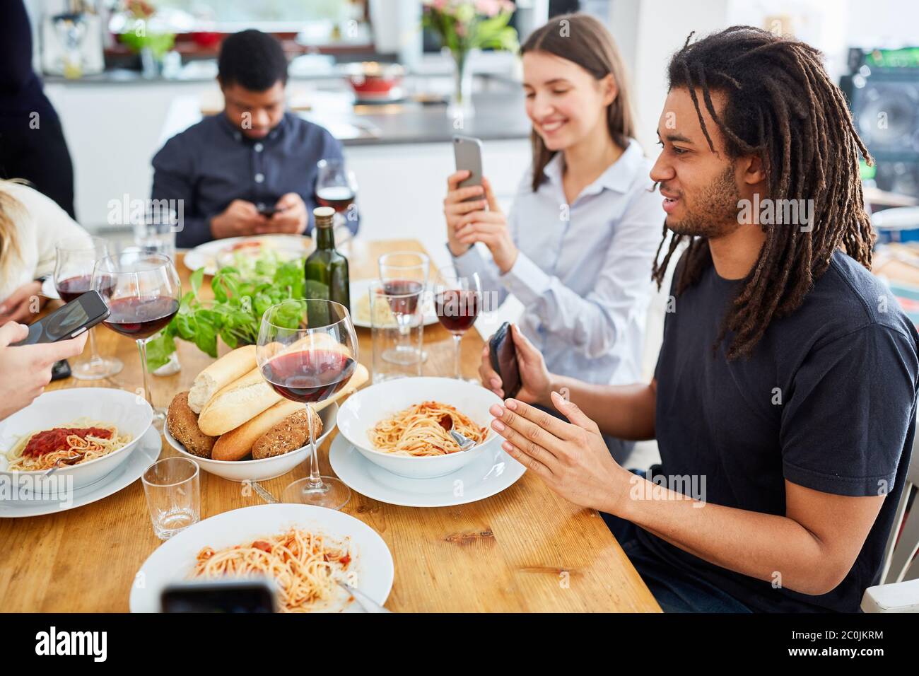 Eine Gruppe von Menschen, die zusammen am Tisch essen, schaut vor dem Start auf das Smartphone und macht Foodie-Bilder Stockfoto