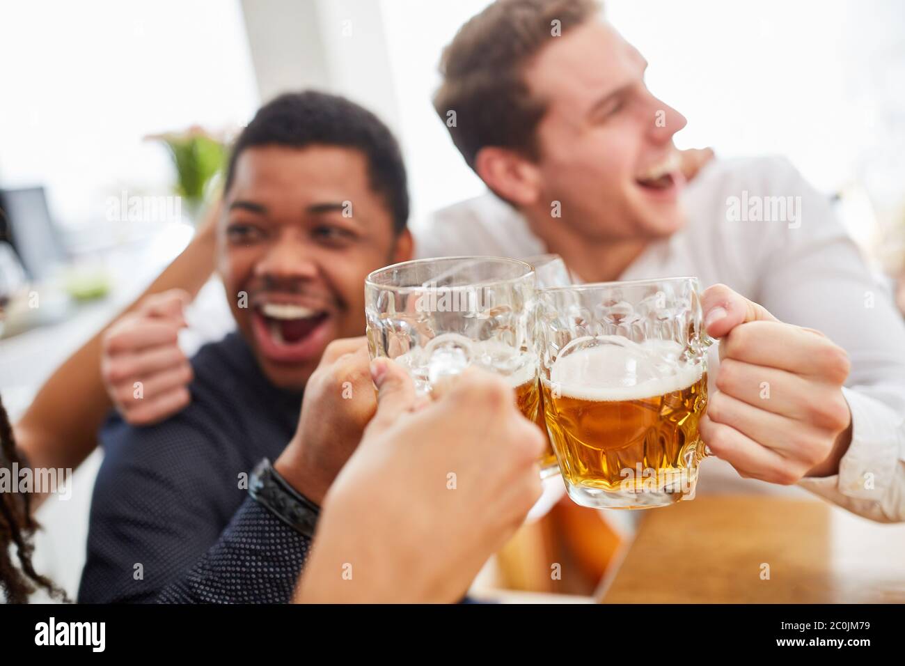 Lachend jubelnde Männer trinken Bier und stoßen sich an, während sie Fußball schauen Stockfoto
