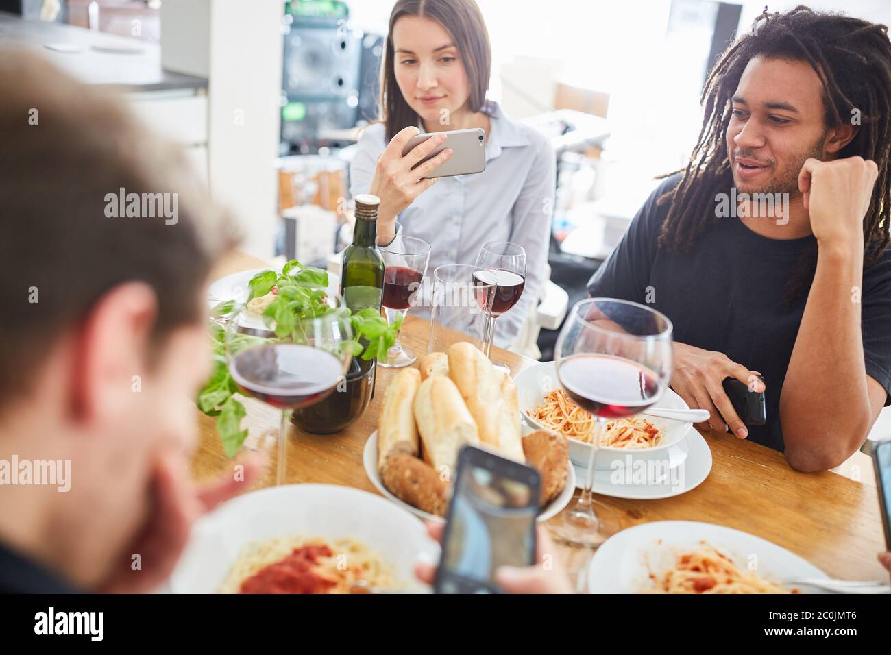 Eine Gruppe von Freunden, die zusammen am Tisch essen, macht vor dem Start Fotos von Foodie und schaut auf das Smartphone Stockfoto